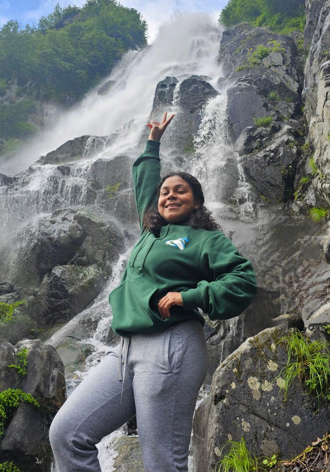 Picture of a smiling SBS employee standing in front of a waterfall.